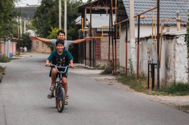 Genç çocuğun iki mutlu arkadaşı yaz tatilinde bisiklet sürerler. Şymkent, Kazakistan - 12 Temmuz 2024