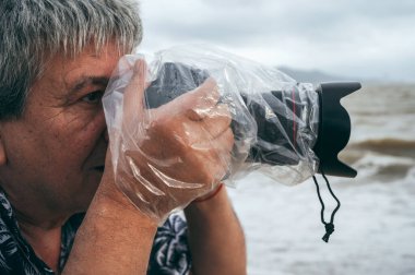 Profesyonel erkek fotoğrafçı, doğada su geçirmez plastik torba içinde dijital kamerayla fotoğraf çeker.