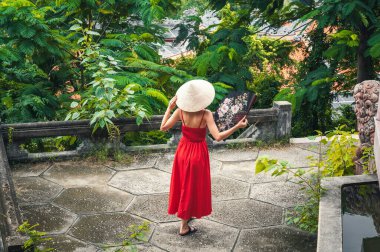 Vietnam 'da bir bahçede yelpazesi olan Vietnamlı non-la şapkalı güzel bir turist kadının arkasında. Asya 'da turizm ve seyahat