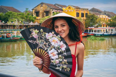 Vietnam 'da Hoi An' da Vietnam 'da bir köprüde yelpaze takmış Vietnam şapkalı mutlu bir genç bayan turist.