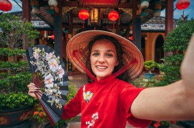 Vietnam 'da Asya' da bir tapınakta Vietnamlı şapkalı mutlu genç bir turistin selfie portresi.