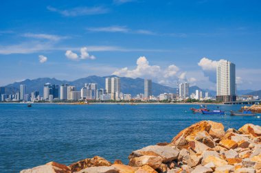 Sahilin arka planında büyük kayalar, Vietnam tekneleri, dağlar ve Nha Trang, Vietnam 'daki yüksek binalar.