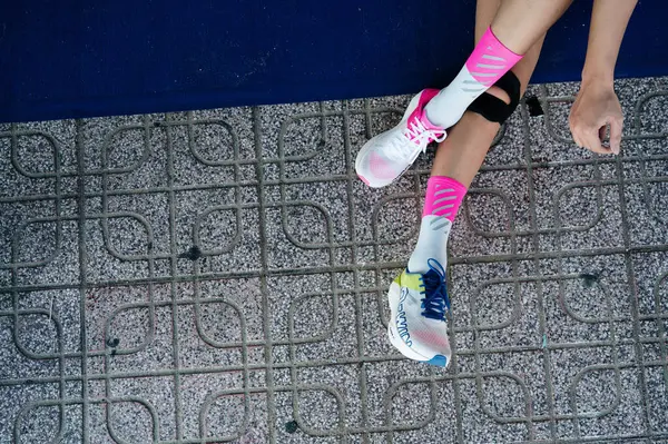 Nha Trang, Khanh Hoa Eyaleti, Vietnam - 11 Ağustos 2024: Esnek ve etkin giyimli kadın ve spor ayakkabıları gri arka planda bacakları esnetiyor, motivasyon