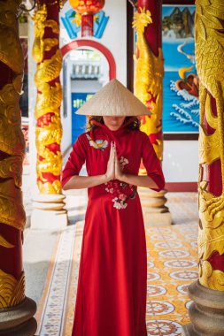 Geleneksel Vietnamlı şapkalı ve kostümlü Asyalı genç bir kadın Vietnam 'da bir Budist tapınağında dua ediyor.