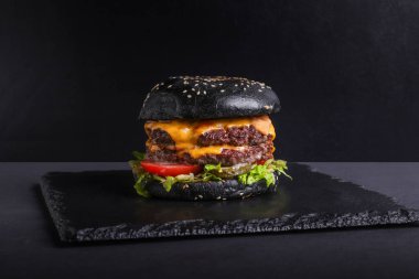 Siyah arka planda bir burger. Kes ve doldur. Et ve salata. Fast food minimalizmi. Abur cubur. Kolesterol. Turba tahtası. Yemek standı Üst Manzara. Düz.