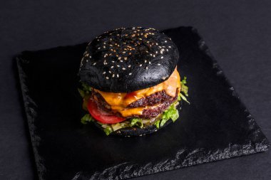 Siyah arka planda bir burger. Kes ve doldur. Et ve salata. Fast food minimalizmi. Abur cubur. Kolesterol. Turba tahtası. Yemek standı Üst Manzara. Düz.
