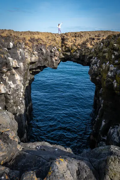 Woman posing on a stone arch in the sea in Arnarstapi, Iceland