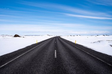 İzlanda 'da omzunda karla yapayalnız siyah asfalt yol