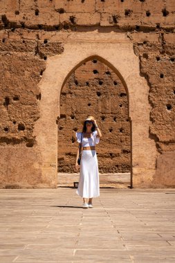 Beyaz elbiseli ve Şapkalı Genç Koyu Saçlı Kadın El Badii Sarayı Marakeş Bahçesinde poz veriyor.