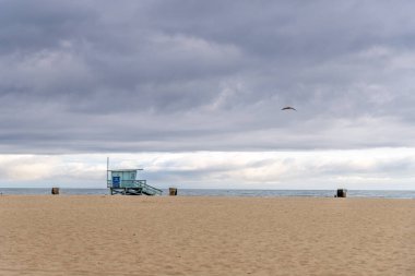 Santa Monica Sahili, Kaliforniya 'da karamsar ve dramatik bir gökyüzüne karşı inşa edilmiş bir cankurtaran kulesinin bulunduğu güzel sakin bir sahil manzarası.
