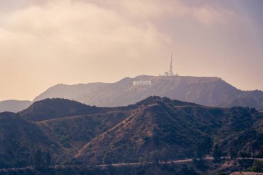 Amerika 'nın Los Angeles kentindeki Hollywood mektuplarının uzak görüşüyle arka planda uzanan dramatik ve bulutlu bir gökyüzü tarafından güzelce tamamlanmış görkemli bir dağ sırasının yatay görüntüsü.