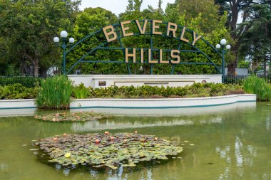 Huzurlu bir parkta, canlı nilüferlerle süslenmiş sevimli bir gölet ve Los Angeles, Kaliforniya 'da Beverly Hills kelimelerini gururla gösteren bir tabela var.