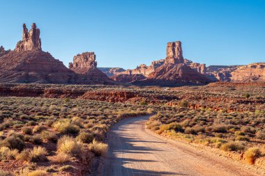 Engin çöl manzarası boyunca uzanan uzun, dolambaçlı toprak bir yol arka planda yükselen görkemli dağlarla Utah 'ta Sunset' teki Tanrıların Yolu Vadisi 'nin çarpıcı manzarasını yaratır.