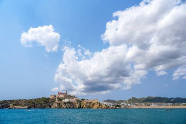 Mavi sular ve canlı bir gökyüzü tarafından çerçevelenmiş kayalık bir çıkıntı üzerinde tarihi bir şatonun yer aldığı nefes kesici kıyı manzarası. Eivissa, İbiza, İspanya.