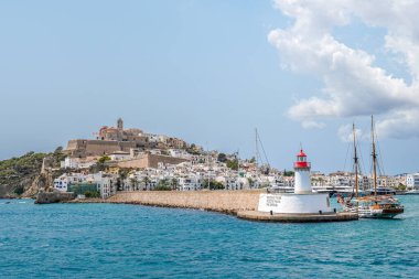 Ibiza 'nın büyüleyici limanı, deniz feneri ve tepenin üzerinde berrak mavi sularla çevrili tarihi eski bir kasabanın görüntüsü..
