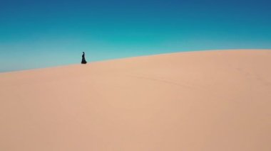 Geleneksel siyah abaya 'da genç bir kadının Boş Bölge Çölü' ndeki kum tepelerinde yürüyüşünü izleyen bir dronun hava görüntüsü. Abu Dabi, BAE. Yüksek kalite 4k görüntü