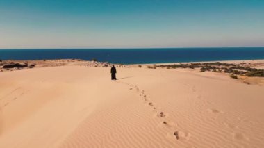 Geleneksel BAE elbisesi giyen Arap kadın - abaya arkasında dağlar olan bir çölde yürüyor. Yüksek kalite 4k görüntü