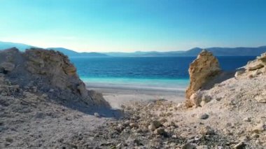 Take a breathtaking aerial tour of a tropical paradise with this stunning drone shot. Soar above a crystal-clear blue ocean as it meets a pristine white beach surrounded by majestic mountains. This