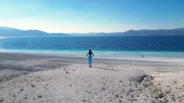 Escape to a tropical paradise as we capture a young woman standing on a pristine white beach, surrounded by the brilliant blue sea. Dressed in a stunning blue cloth, she takes in the breathtaking