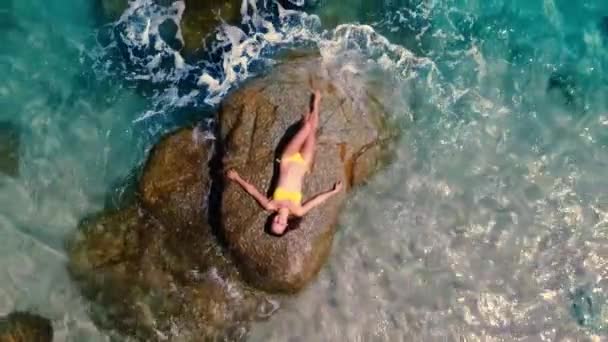 穿着黄色泳衣的年轻漂亮性感的女孩在水晶般碧绿的大海中在岩石上摆姿势 这让人眼前一亮 是的高质量的4K镜头 — 图库视频影像
