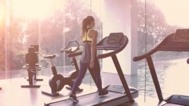 Kadın panoramik pencerede koşu bandında koşuyor ve sabah spor salonunda güneş doğuyor. Sağlıklı yaşam tarzı kavramı. Yüksek kalite 4k görüntü