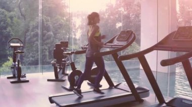 Kadın panoramik pencerede koşu bandında koşuyor ve sabah spor salonunda güneş doğuyor. Sağlıklı yaşam tarzı kavramı. Yüksek kalite 4k görüntü