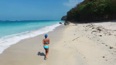 Güzel otantik kadın Bali adasındaki boş kumsalda sörf dalgalarıyla koşuyor. Yüksek kalite 4k görüntü