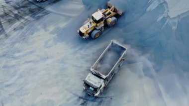 Ezilmiş taş ocağındaki bir çöp kamyonuna ezilmiş taş yükleyen bir yükleyicinin havadan aşağı görüntüsü. Yüksek kalite 4k görüntü