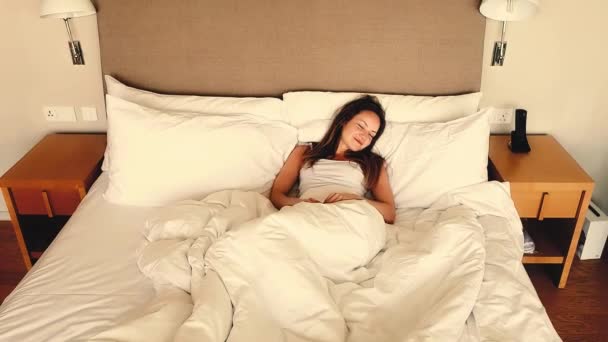 ベッドに横たわって目を覚ます幸せな眠った若い女性 居心地の良い寝室で早朝を楽しみながら伸びるポジティブな美少女 高品質の4K映像 — ストック動画