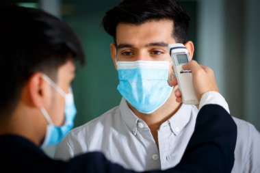 Kapatın, resepsiyonist ve konuk otel resepsiyonunda yüz maskesi takıyor. Alnında vücut ısısı kontrolü, kovid 19 ve koronavirüs enfeksiyonu koruma konsepti kullanın.