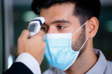 Kapalı, yüz maskesi takan konukların seçici odak yüzü, resepsiyonistin eli. Alnında vücut ısısını kontrol edin. Otel Covid 19 ve Coronavirus enfeksiyon koruma konsepsiyonunda.