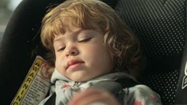 Beautiful toddler girl falling asleep while sitting on a car seat inside moving car