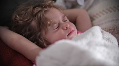 Beautiful little girl sleeping on top of blankets and moves her eyes for a moment