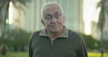 Yaşlı bir adamın parkta komik bir ifadeyle kameraya baktığı orta boy bir fotoğraf.