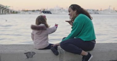 Slow motion of a mother and little daughter sitting by the water having a conversation