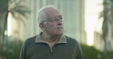 Slow motion medium shot of a senior man looking around park with expression of confusion and doubt