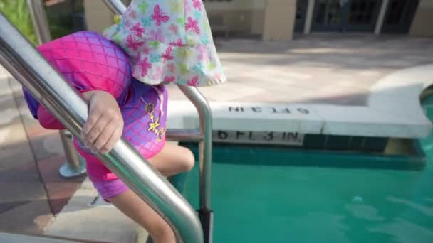 Маленькая Девочка Поплавками Пытается Залезть Бассейн Лестнице Смотрит Камеру Улыбается Стоковое Видео