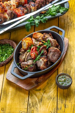 Barbekü ızgara et, domuz eti, tavuk ve sebze, dökme demir tavada. Sarı ahşap arka planda ızgara şişler. Üst görünüm.