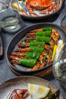 Baharatlı sarımsaklı kaplan karides kızartma tavasında karides ve siyah masada limon yaprağı..