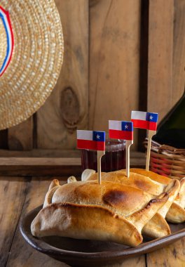 Şili 'nin bağımsızlık günü kavramı. fiestas patrias. Tipik pişmiş empanadas de pino, şarap ya da chicha, şapka ve emboque. 18 Eylül partisinde yemek ve içki, ahşap arka plan.