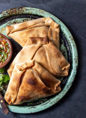 Tipik pişmiş empanadas de Pino, klasik denemede peber soslu, siyah taş arka planlı. Bağımsızlık Günü partisi için geleneksel Şili yemekleri.