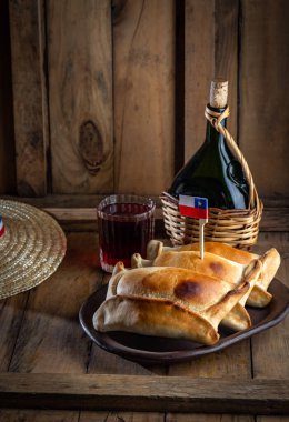 Şili 'nin bağımsızlık günü kavramı. fiestas patrias. Tipik pişmiş empanadas de pino, şarap ya da chicha, şapka ve emboque. 18 Eylül partisinde yemek ve içki, ahşap arka plan.