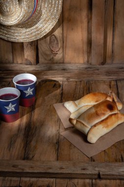 Şili 'nin bağımsızlık günü kavramı. fiestas patrias. Tipik pişmiş empanadas de pino, şarap ya da chicha, şapka ve emboque. 18 Eylül partisinde yemek ve içki, ahşap arka plan.