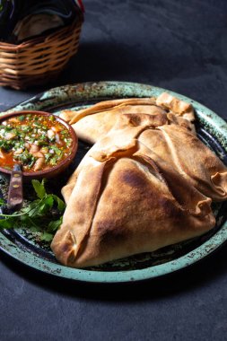 Tipik pişmiş empanadas de Pino, klasik denemede peber soslu, siyah taş arka planlı. Bağımsızlık Günü partisi için geleneksel Şili yemekleri.