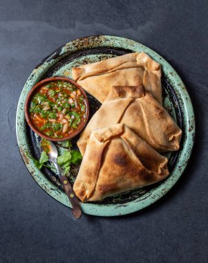 Tipik pişmiş empanadas de Pino, klasik denemede peber soslu, siyah taş arka planlı. Bağımsızlık Günü partisi için geleneksel Şili yemekleri.