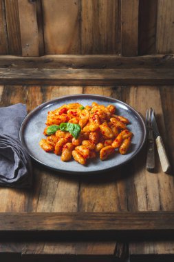 Domates soslu geleneksel İtalyan patatesi Gnocchi ve ahşap arka planda mavi tabakta taze fesleğen.