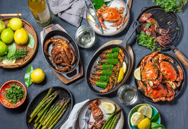 Set table with seafood dishes - cooked crabs, tiger shrimps, grilled octopus and squids on cast iron grilled pans and plates, White wine. Top view.