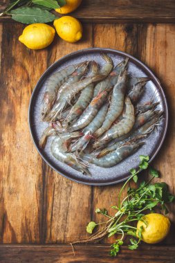 Gri tabakta çiğ karides, limon ve kişniş. Üst manzara, ahşap arkaplan.