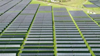 Yeni bir güneş çiftliğinin üst görüntüsü. Yeşil alanın yanındaki modern fotovoltaik güneş panellerinin sıraları
