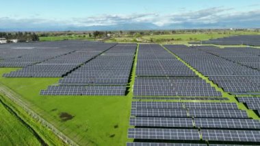Yeni bir güneş çiftliğinin üst görüntüsü. Yeşil alanın yanındaki modern fotovoltaik güneş panellerinin sıraları